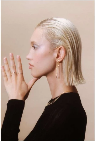 Profile portrait of a blonde woman wearing delicate gold rings and earrings against a neutral studio background