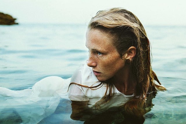 Woman with freckles in ocean, wearing a white dress, fair complexion, wet hair, looking left. Soft light, summer vibe, shallow depth of field.