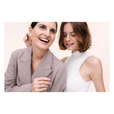 Two smiling adult women in a medium shot, one wearing a blazer, against a cream background, creating a happy and friendly visual.