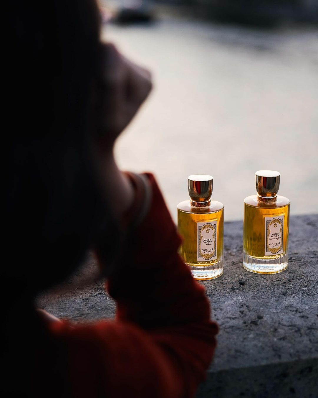 Two perfume bottles on a stone ledge with an out-of-focus person in the foreground by photographer Lucie Sassiat.