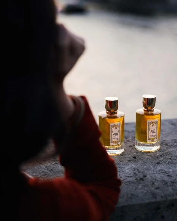 Two perfume bottles on a stone ledge with an out-of-focus person in the foreground by photographer Lucie Sassiat.