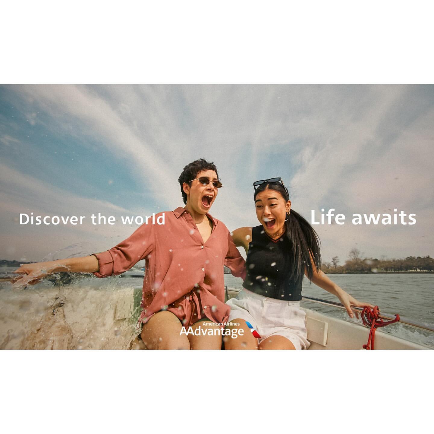 Two cheerful people, an adult male and female, express excitement on a boat under a sky with bright clouds over the water.