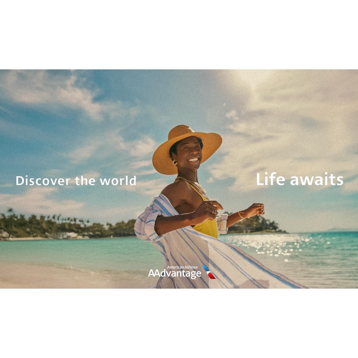 A happy black woman in a hat and swimwear walks on a white sand beach with turquoise water on a sunny day in a travel advertisement.