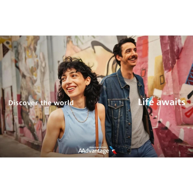 Smiling woman and man walk along a graffiti-covered urban alleyway. They are looking toward the distance. American Airlines logo is displayed.