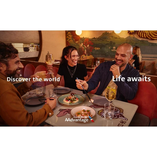 Three people laughing at a restaurant table with appetizers, drinks, and the American Airlines AAdvantage logo prominently displayed.