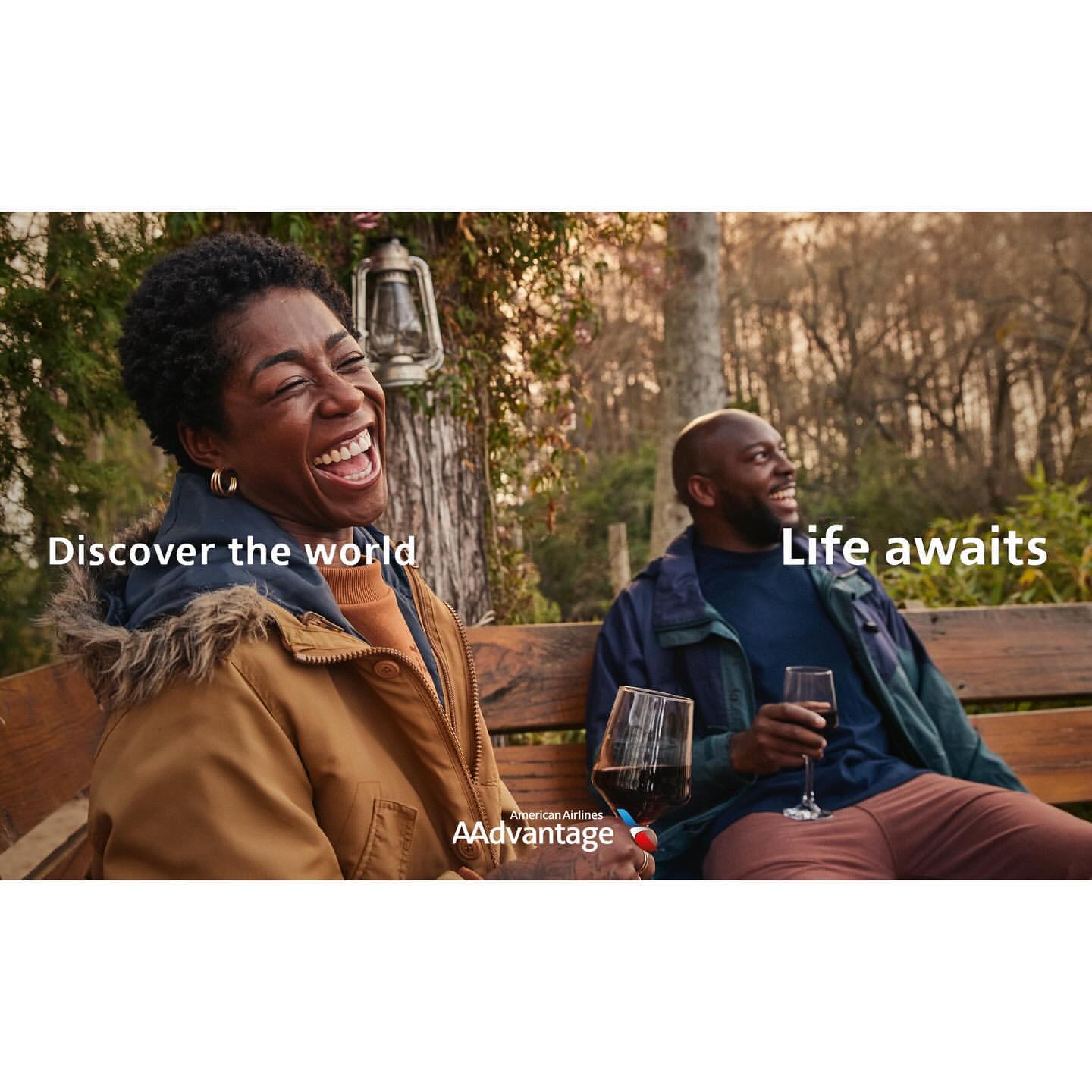 Two African American adults relax outside with wine glasses on a bench, enjoying a candid moment amid a natural outdoor setting.
