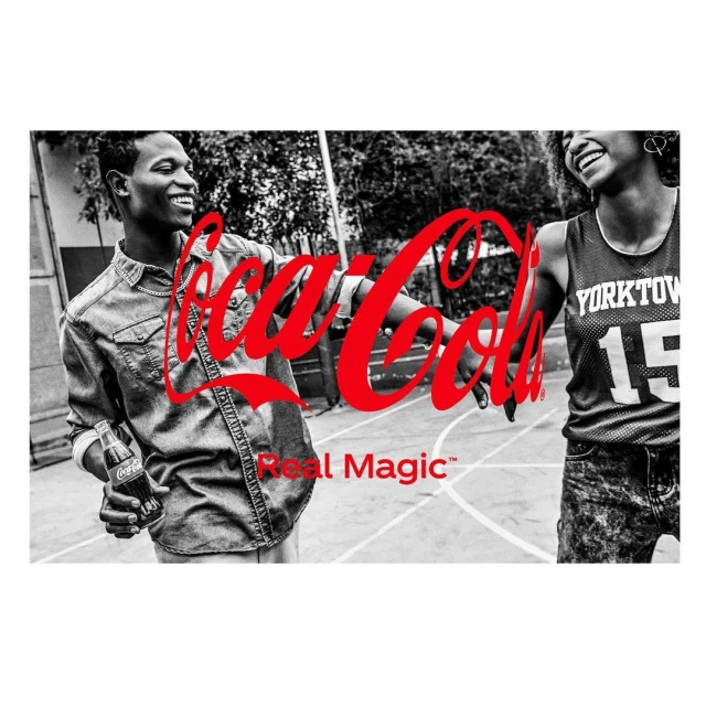 Two smiling young adults in black and white hold a Coca-Cola bottle, with the Coca-Cola logo and Real Magic tagline in red.