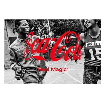 Two smiling young adults in black and white hold a Coca-Cola bottle, with the Coca-Cola logo and Real Magic tagline in red.