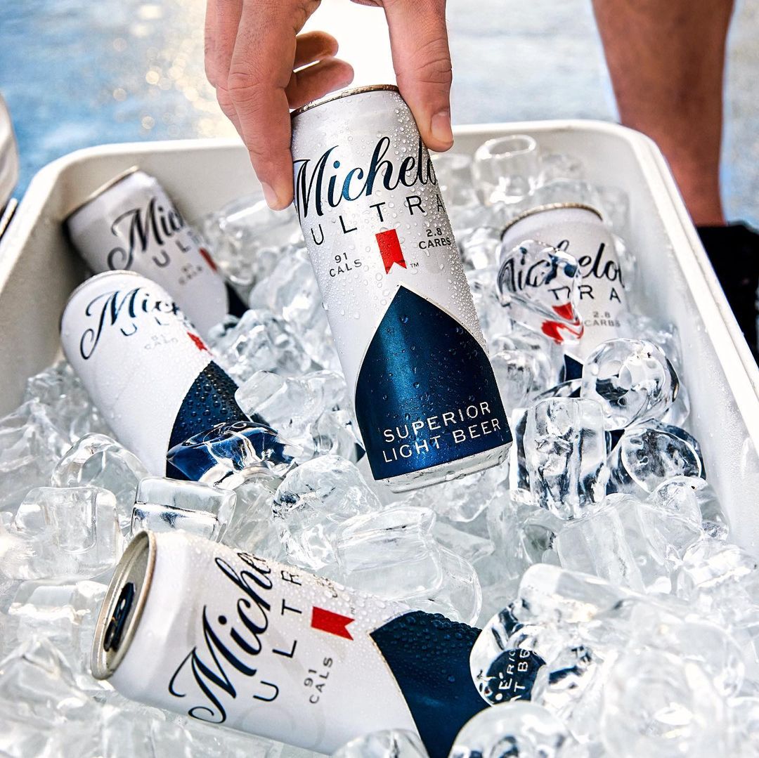 Hand holding chilled Michelob Ultra beer can in ice-filled cooler. Cold beer cans for refreshment, party, and beverage photography.