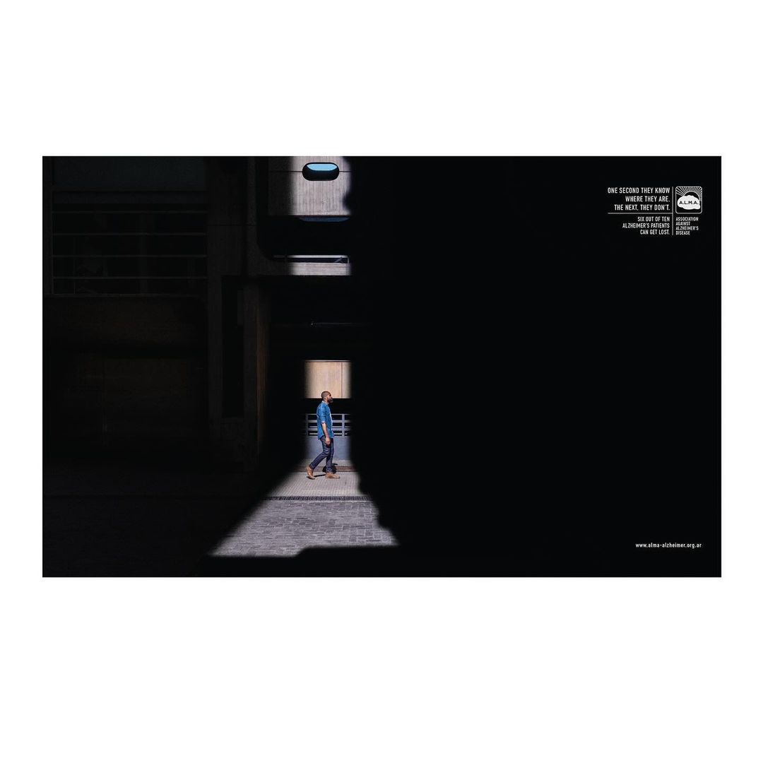 A man walking through a narrow shaft of light in a dark brutalist architectural corridor by Lucila Blumencweig.