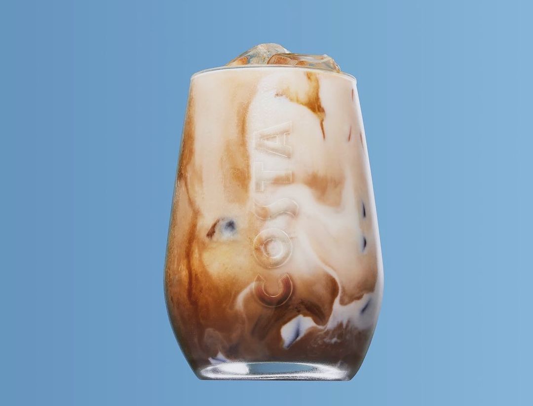 Iced coffee drink with Costa Coffee logo in a clear glass against a light blue background. Close-up studio shot of the drink.