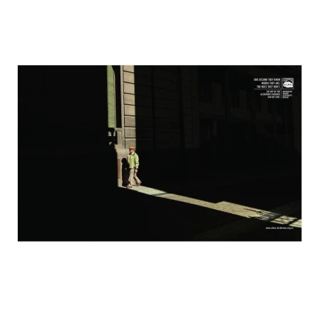 Young boy walks in a beam of light on a dark city street, creating strong contrast and shadows on the surrounding buildings.