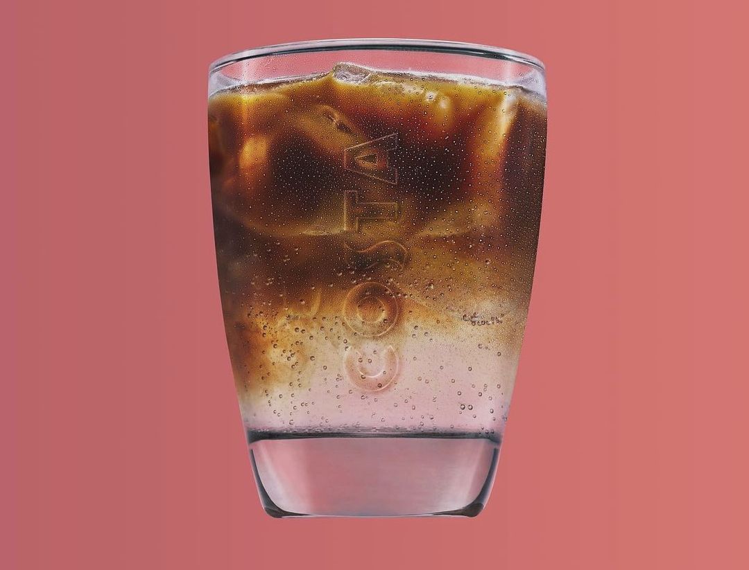 A glass of iced coffee with the Costa Coffee logo on a pink background. Refreshing beverage with visible condensation.