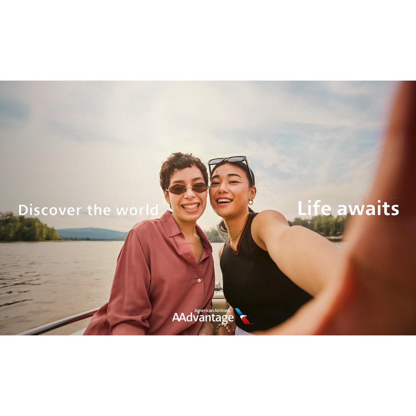 Two women smile at the camera on a boat with a lake and trees visible in the background, promoting American Airlines AAdvantage.