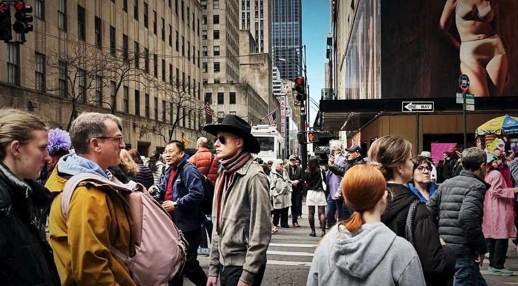 Street scene captures diverse group of people walking among tall buildings on a cloudy day in a bustling urban environment.