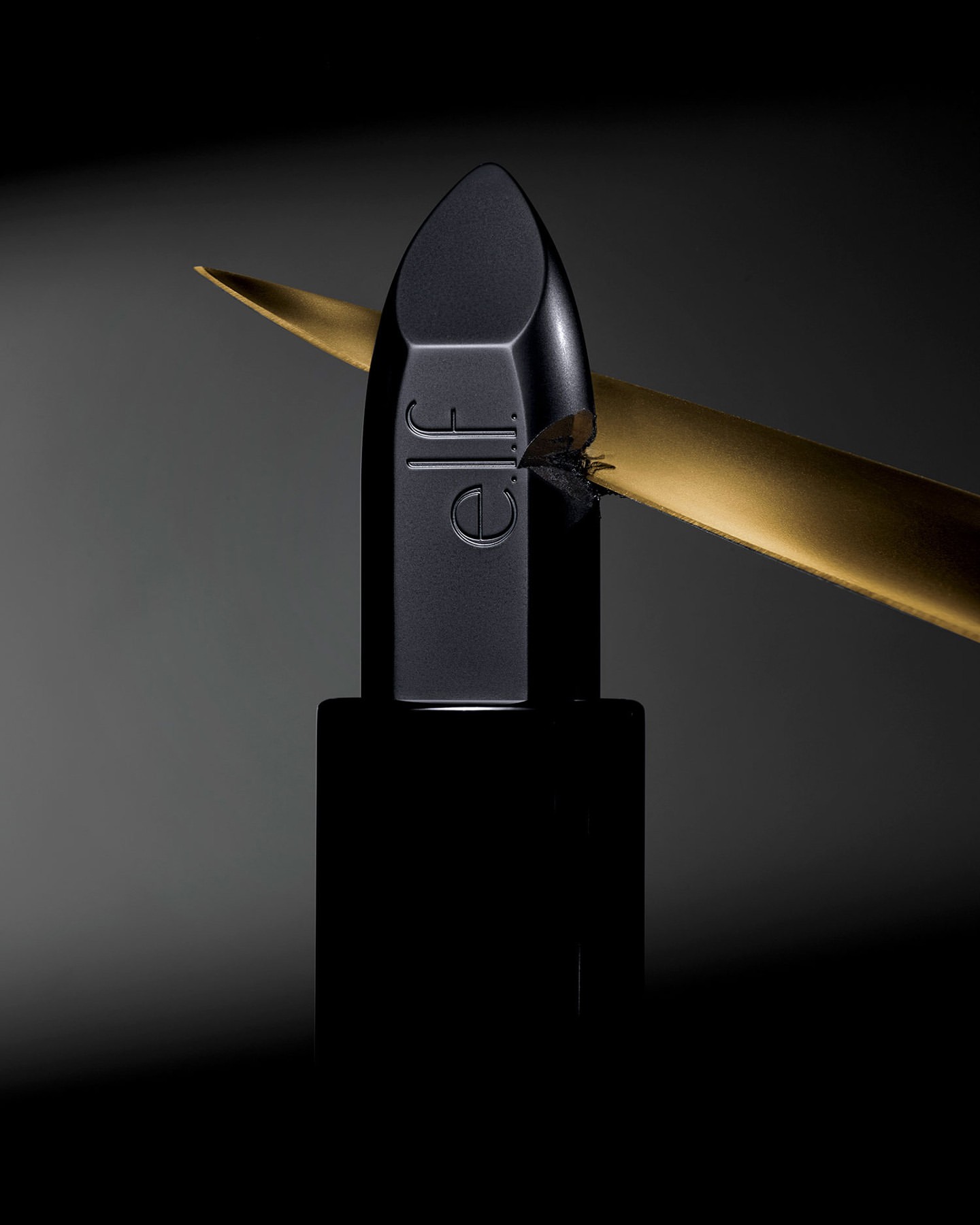 A black lipstick from e.l.f. Cosmetics is presented with a gold accent on a smooth grey gradient background in a product photography style.