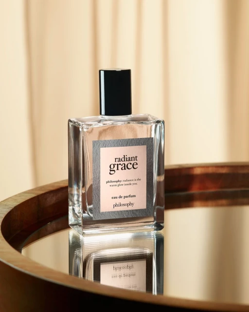 Close-up studio shot of a bottle of Radiant Grace eau de parfum by Philosophy on a reflective surface with a neutral backdrop.