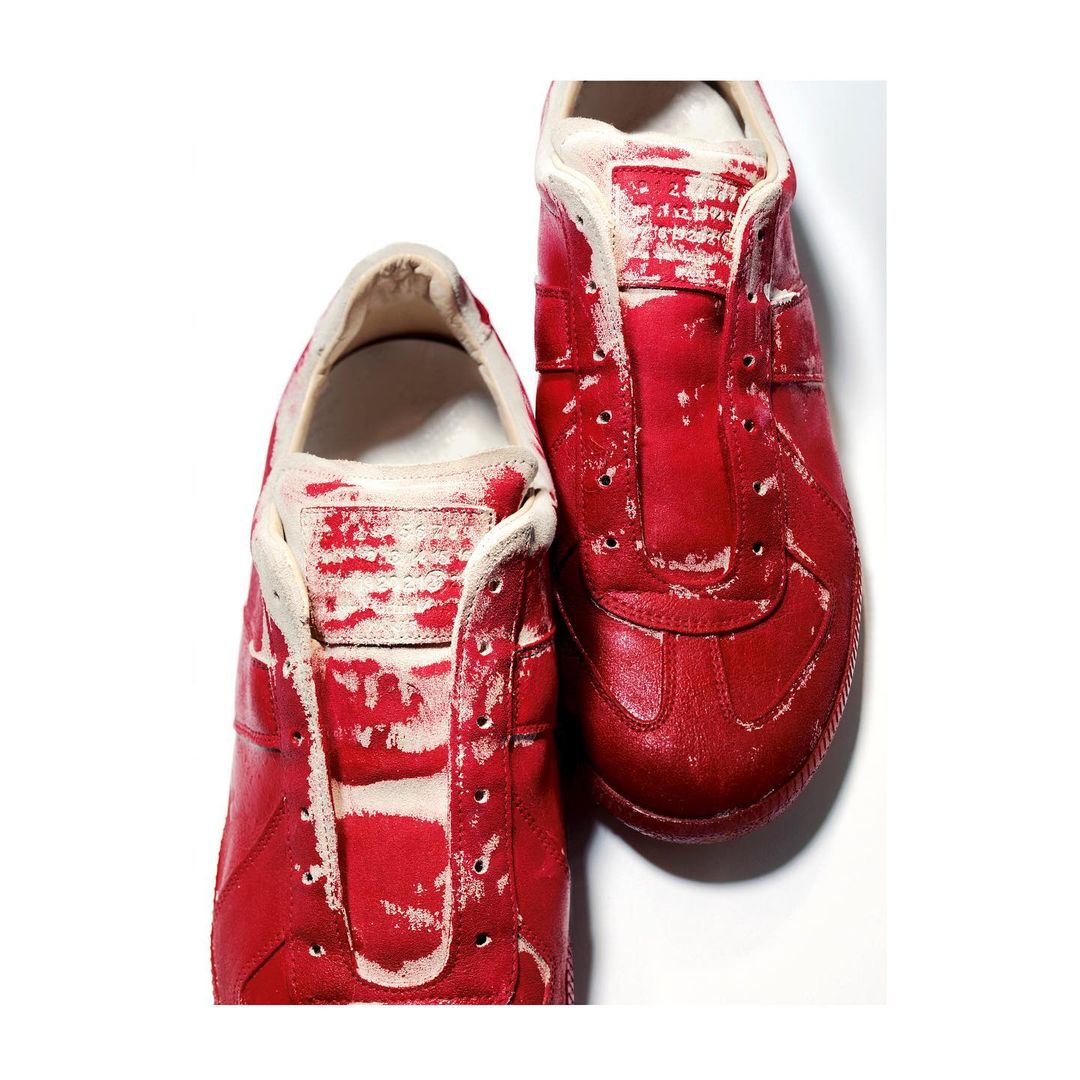 Two red, low-top, lace-less athletic shoes with scuff marks are displayed on a white surface in a studio product shot.