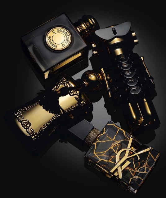 Four black and gold perfume bottles arranged diagonally on a reflective black surface, creating a luxurious and artistic composition.