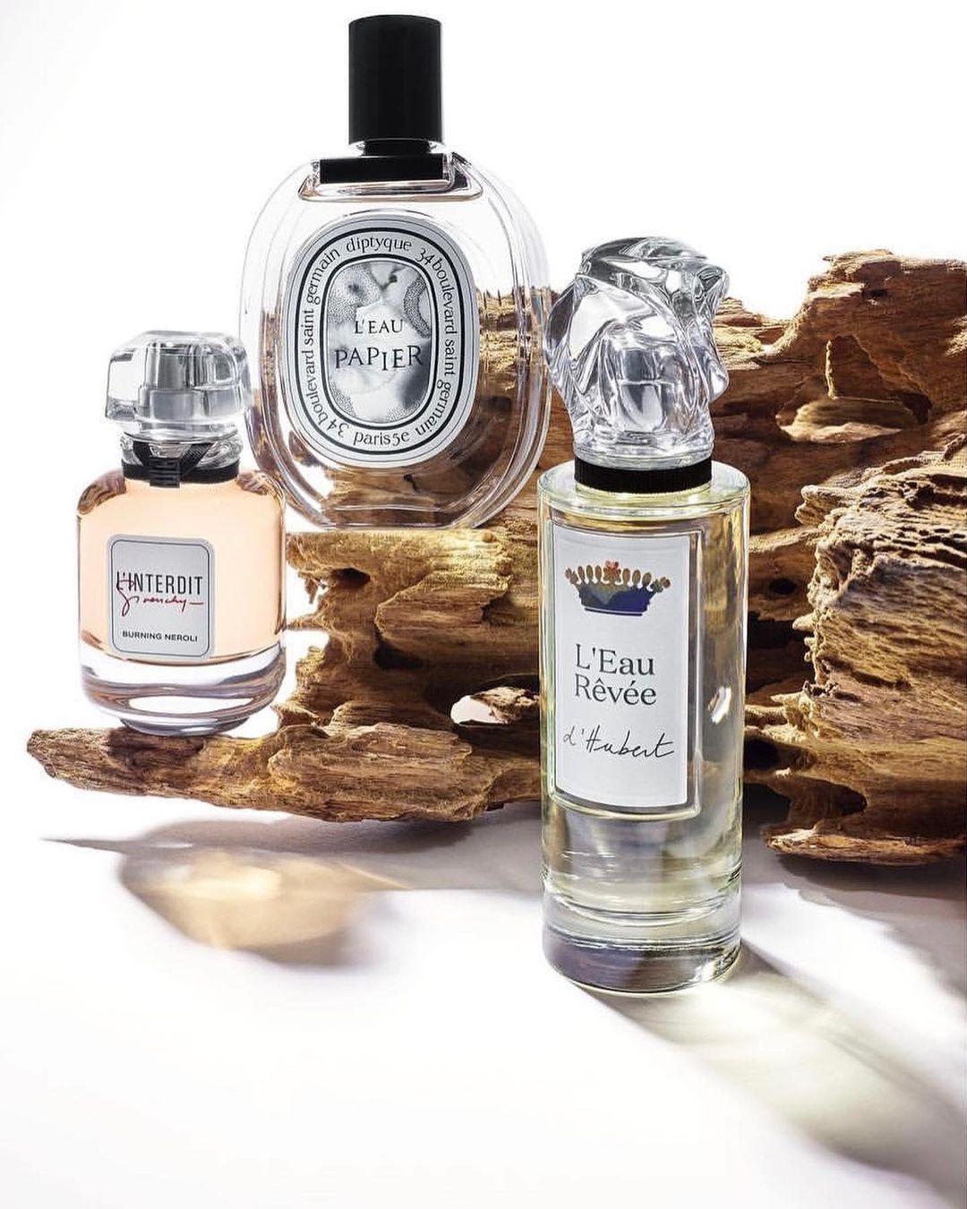Three perfume bottles are displayed on a wooden surface. The bottles feature unique designs, including sculptural stoppers, and clear labels.