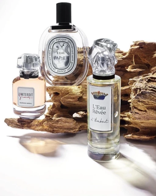 Three perfume bottles are displayed on a wooden surface. The bottles feature unique designs, including sculptural stoppers, and clear labels.