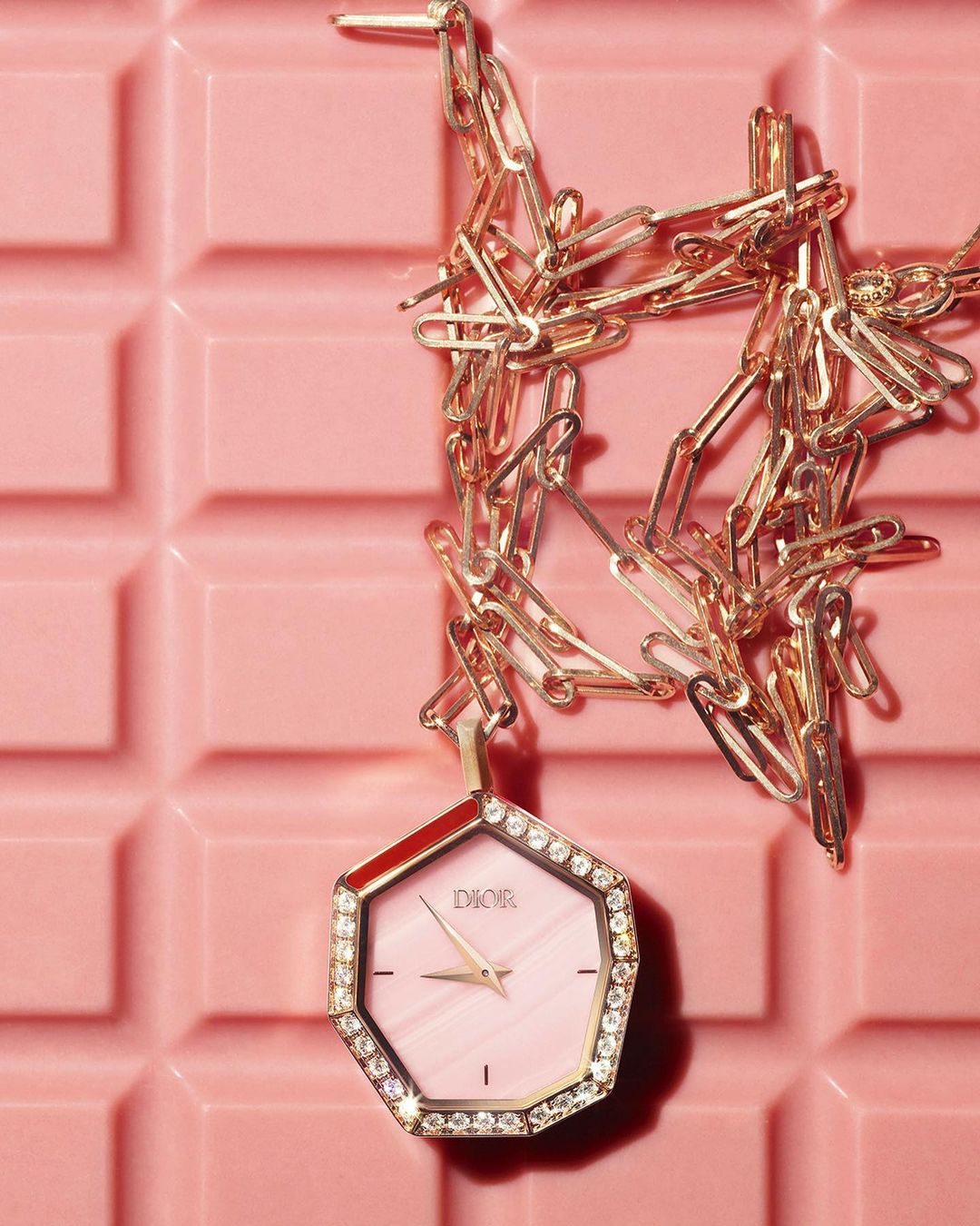 Close-up of a Dior wristwatch with a gold chain on a pink tile surface, highlighting luxury and fashion accessories.