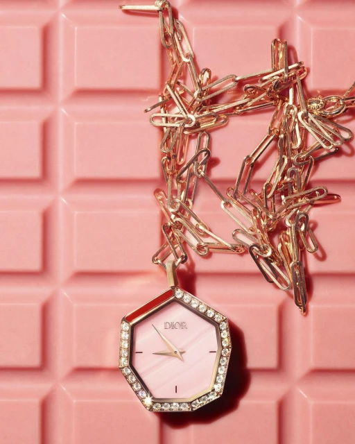 Close-up of a Dior wristwatch with a gold chain on a pink tile surface, highlighting luxury and fashion accessories.