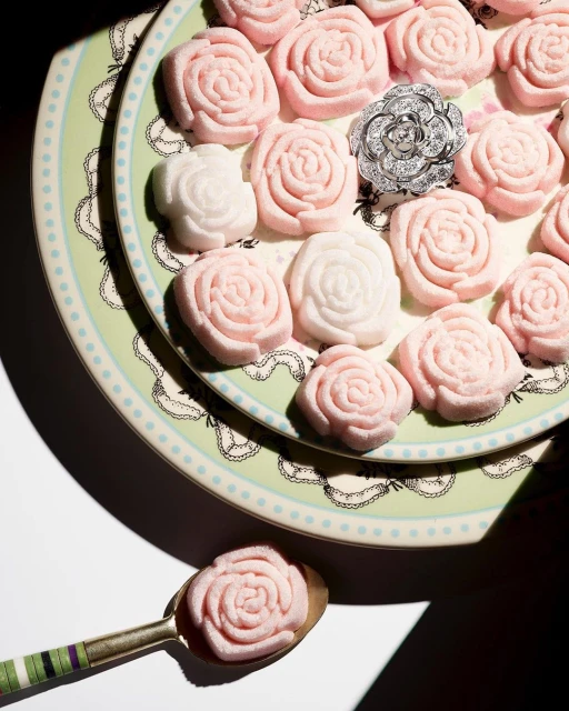 Overhead studio shot of rose-shaped sugar candy in pastel pink and white shades, arranged on decorative plates, plus a silver flower ring.