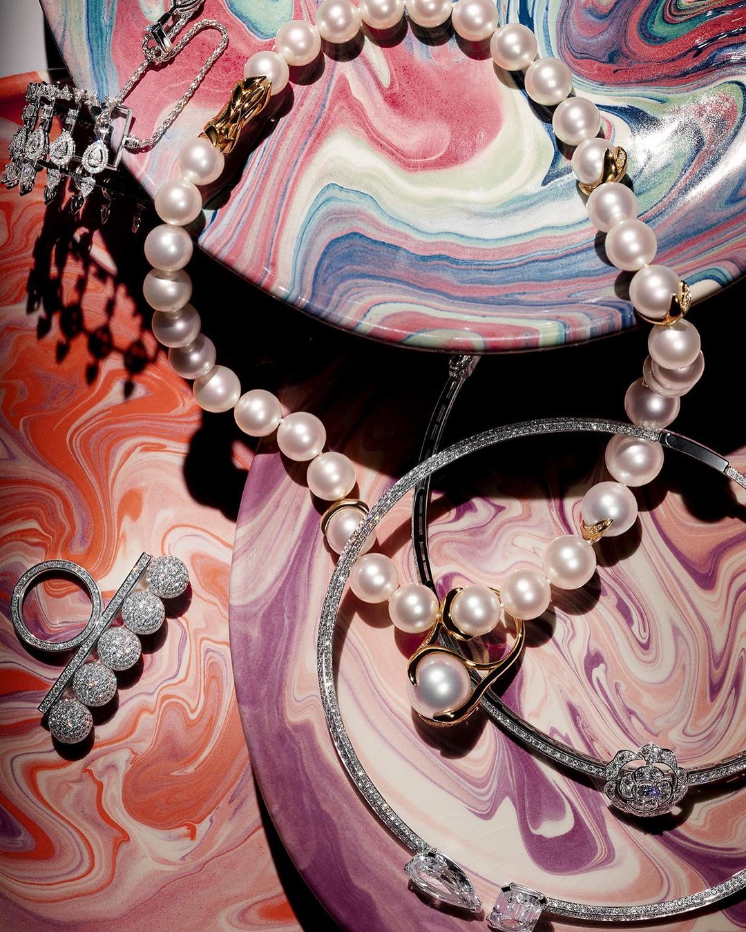 Overhead studio shot of elegant pearl necklaces and diamond rings arranged on a colorful marbled background, jewelry advertisement.