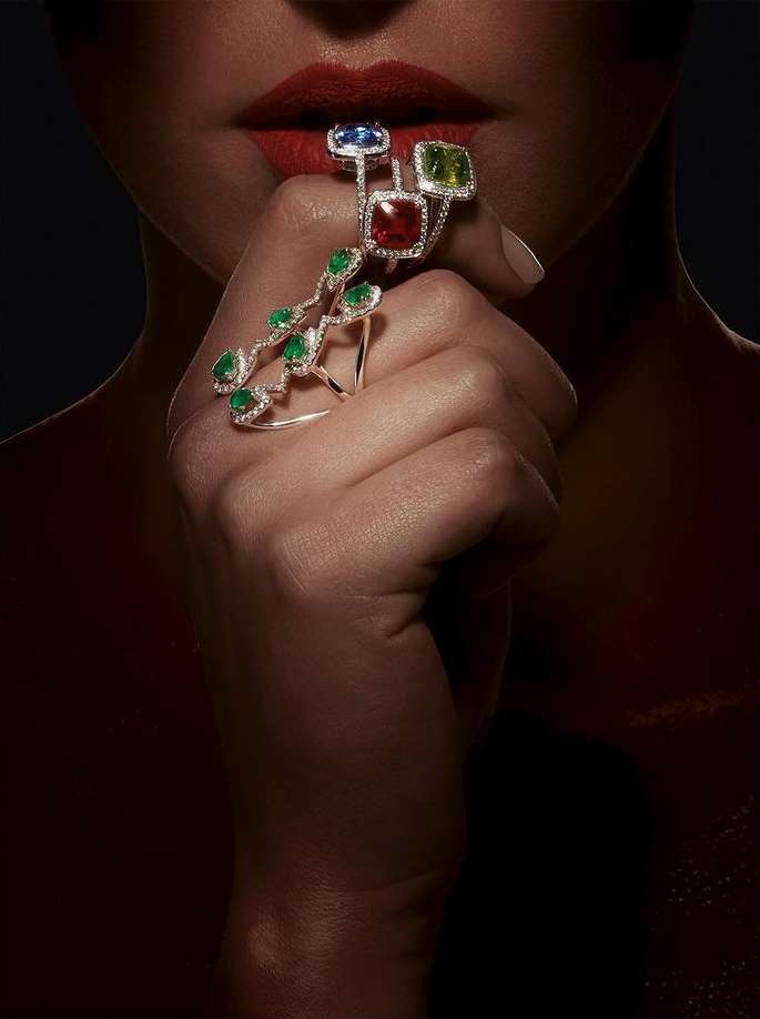 Close-up of a woman's hand adorned with a statement ring featuring multiple gemstones and a vine-like design, lips painted red.