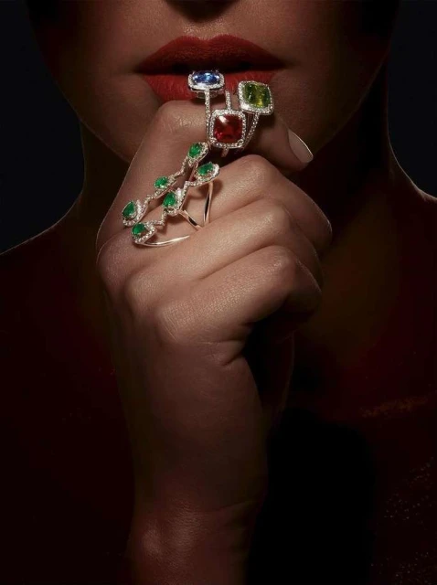 Close-up of a woman's hand adorned with a statement ring featuring multiple gemstones and a vine-like design, lips painted red.