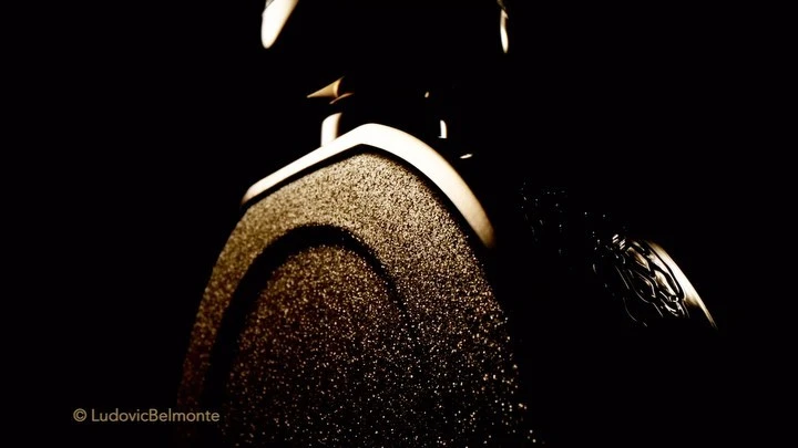 Close-up shot of a microphone with a textured surface and a silver emblem against a stark black background. Studio equipment.