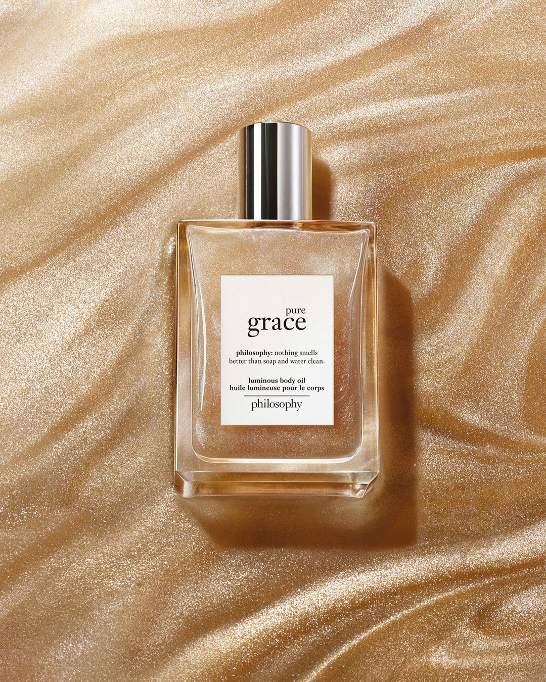 Close-up of a bottle of Philosophy Pure Grace body oil against a golden background, promoting the brand and its luminous body oil.