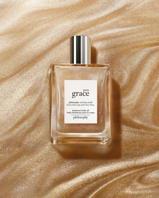 Close-up of a bottle of Philosophy Pure Grace body oil against a golden background, promoting the brand and its luminous body oil.