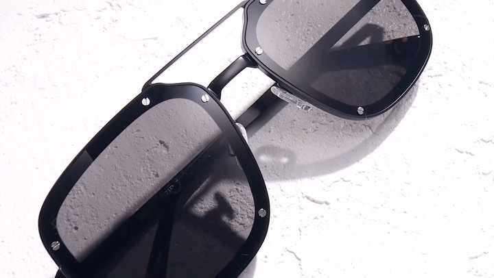 Close-up of sleek black aviator sunglasses with a metal frame, reflecting light on a textured white surface. Stylish eyewear detail.