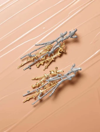 A pair of abstract earrings made of silver and gold metal are displayed on a beige surface, illuminated with soft lighting for a high-fashion look.
