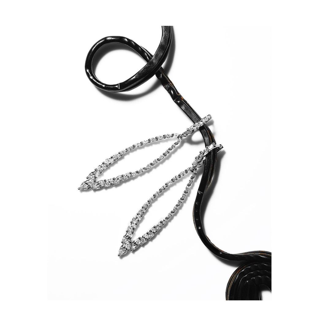 Elegant jewelry flat lay: two silver drop earrings featuring diamond stones, displayed with a black leather cord on white background.