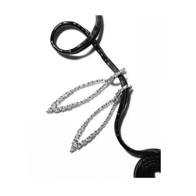 Elegant jewelry flat lay: two silver drop earrings featuring diamond stones, displayed with a black leather cord on white background.