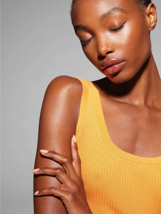Close-up portrait of a woman with closed eyes wearing a yellow ribbed tank top against a plain grey background