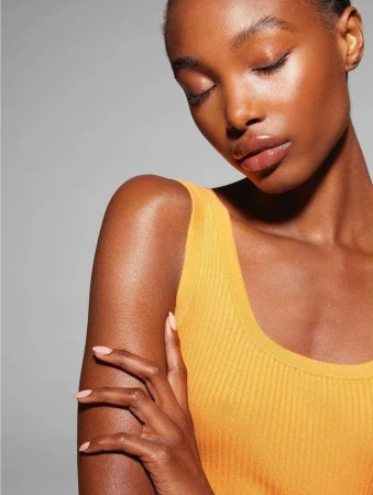 Close-up portrait of a woman with closed eyes wearing a yellow ribbed tank top against a plain grey background