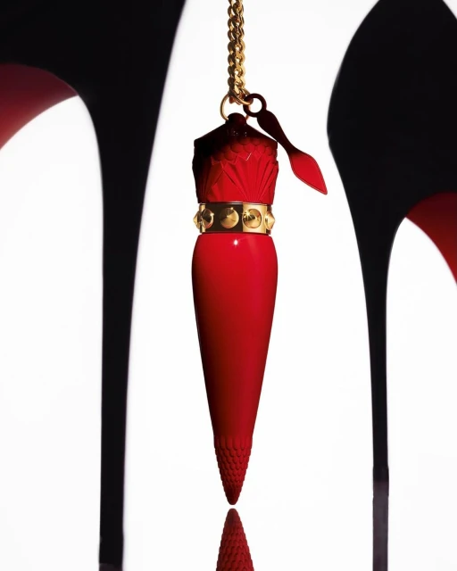 Close-up of red lipstick pendant necklace with gold chain, gold band, and red stiletto high heels on white background.