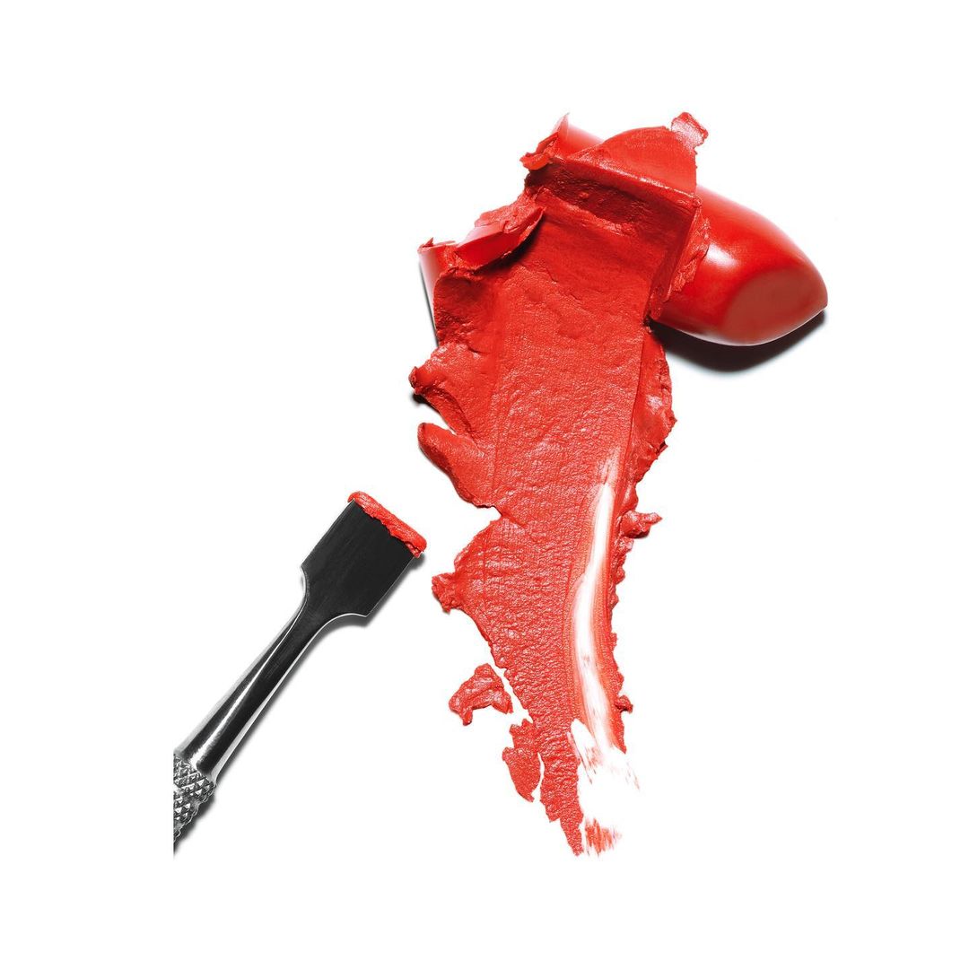 Close-up of vibrant red lipstick swatch and applicator tool on a white background, perfect for beauty or cosmetic advertising.