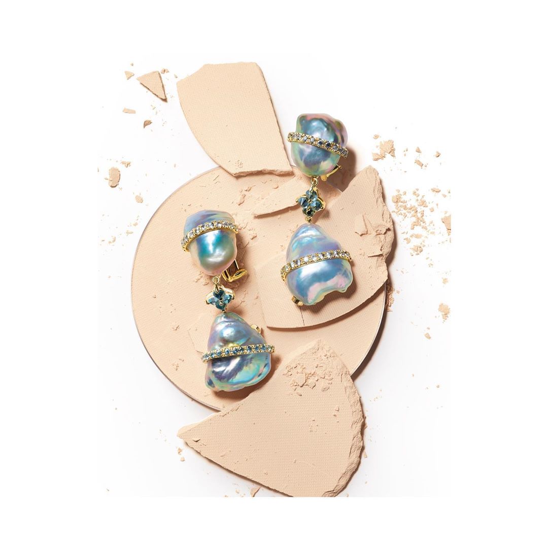 Statement earrings featuring baroque pearls with diamond detailing on a neutral powder background, studio shot for a beauty campaign.