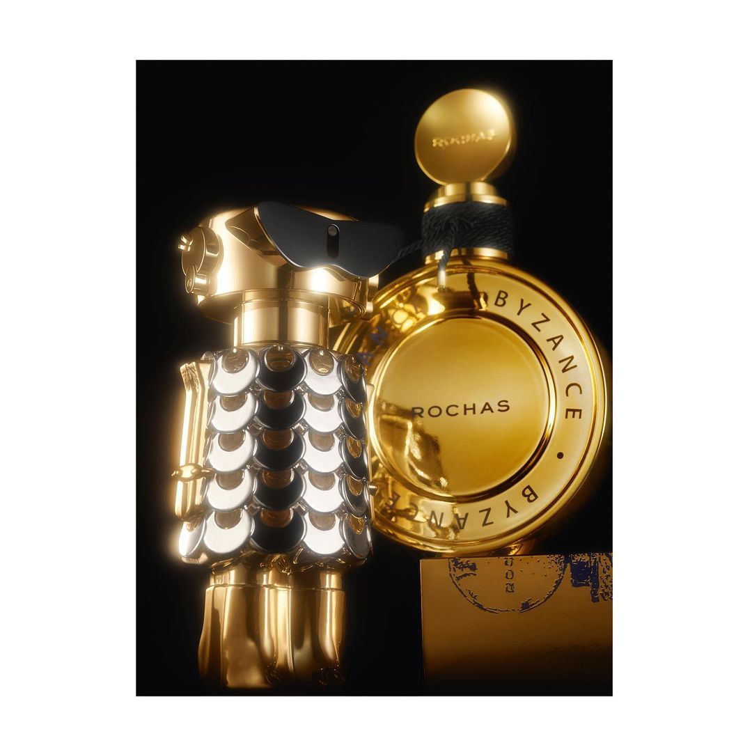 Gold Rochas Byzance perfume bottles with unique, reflective designs stand against a dark backdrop, creating a luxurious beauty still life.