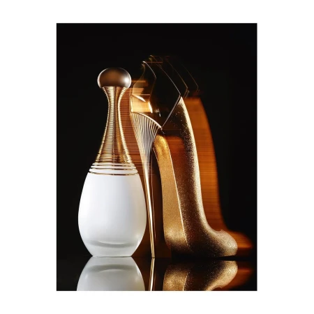 A perfume bottle and a high-heeled shoe shaped bottle displayed against a dark background with dramatic gold lighting.