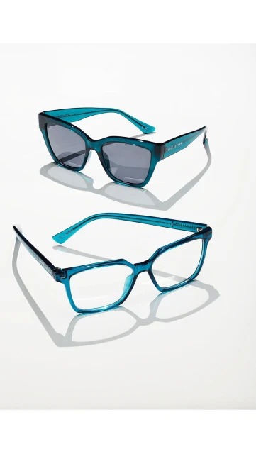 Two pairs of stylish eyeglasses and sunglasses with teal frames are positioned on a white surface, casting distinct shadows.