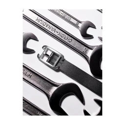 Close-up overhead shot of a black leather belt with a silver buckle arranged among chrome wrenches on white background