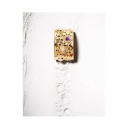 Gold statement cuff bracelet with inset purple and white stones against a white textured background
