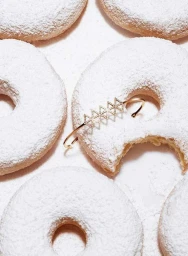 Close-up product shot of a gold diamond bracelet resting on top of powdered sugar donuts against a white background