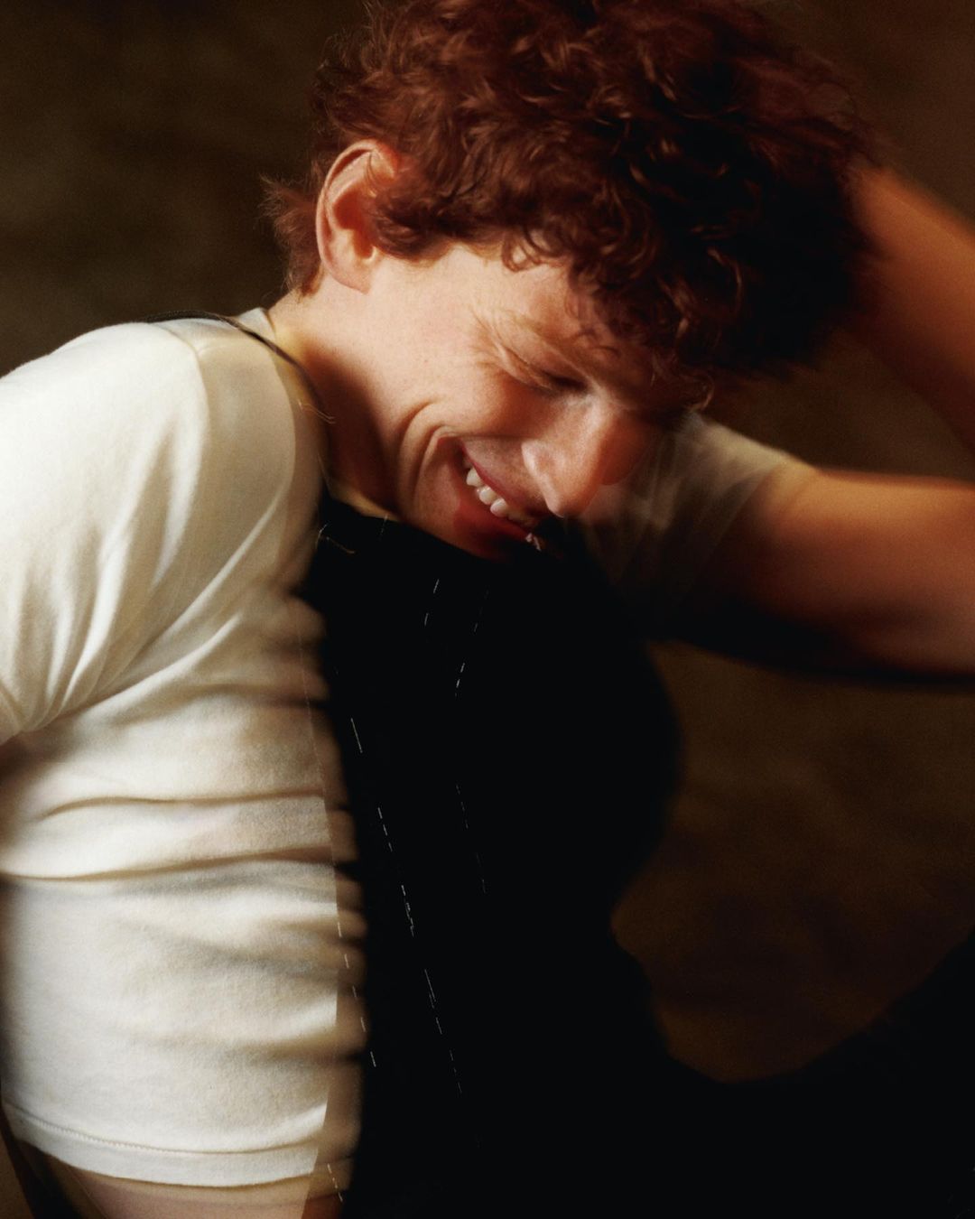 Portrait of a man with curly red hair smiling, wearing a white t-shirt and dark overalls, photographed by Luis Alberto Rodriguez.
